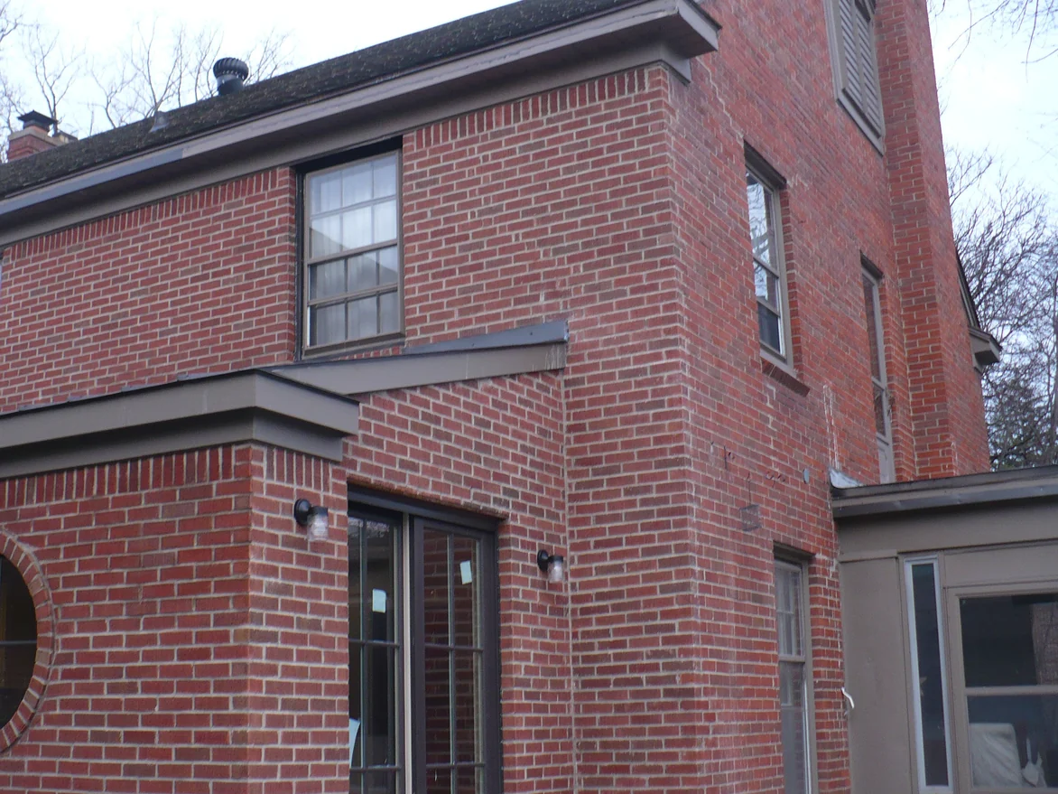 The same outside corner of the house later that winter, the brick on both faces reading as one red range with the round window at the left edge