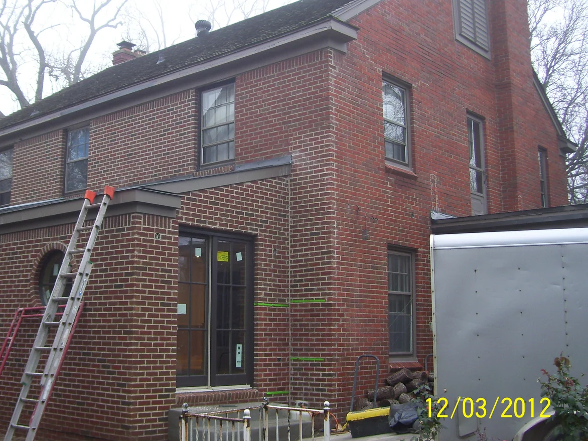 The rear of the house on a bare winter day with an extension ladder against the wall and green tape masking the edge of the brick being worked on