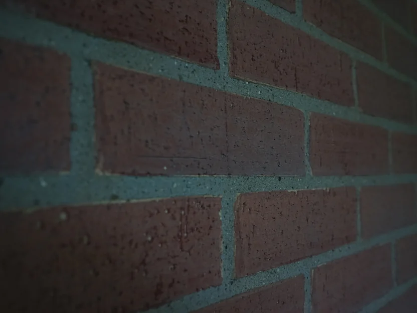 Stained brick at arm's length, the pitted face of each unit and the sand in the mortar joints in focus in the foreground and falling off along the wall