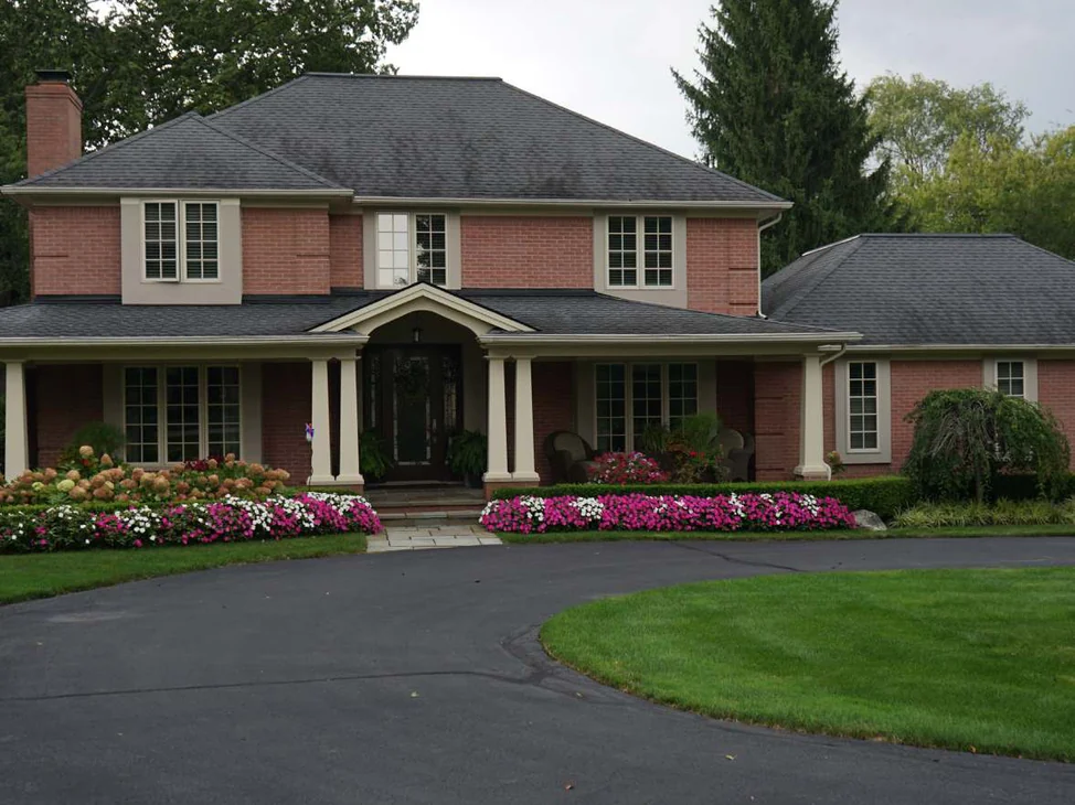 The front of the house in 2019 from across the drive, salmon brick between cream trim and columns, beds of pink and white flowers along the porch