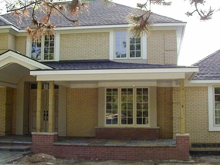 The front of the new house in 2003 in pale yellow brick, bare wood posts holding up the porch roof, red brick at the porch base and raw earth in front