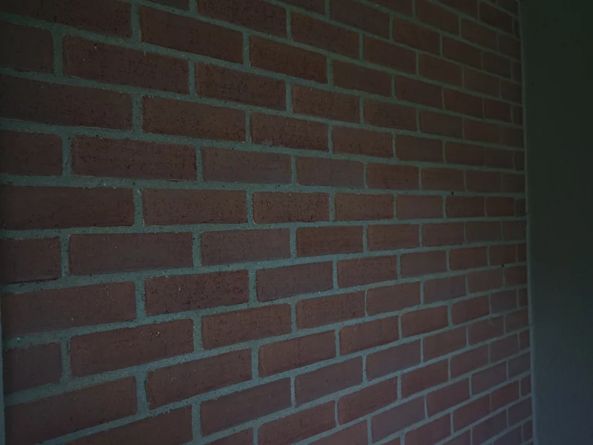 A panel of stained brick between two cream returns, shot at an angle in shade, grey mortar joints and the face texture of each unit showing through the color
