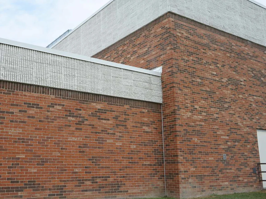 An outside corner of the school in 2019, red brick with brown and buff units carried through the corner under a grey masonry band, a downpipe on the return and mown grass at the base