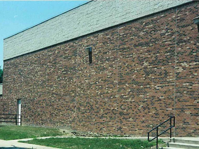 The long side wall of the school in 2002 seen down its length, brick reading red and tan in one range under a grey masonry band, two wall lights and a lower wing set back at the far end