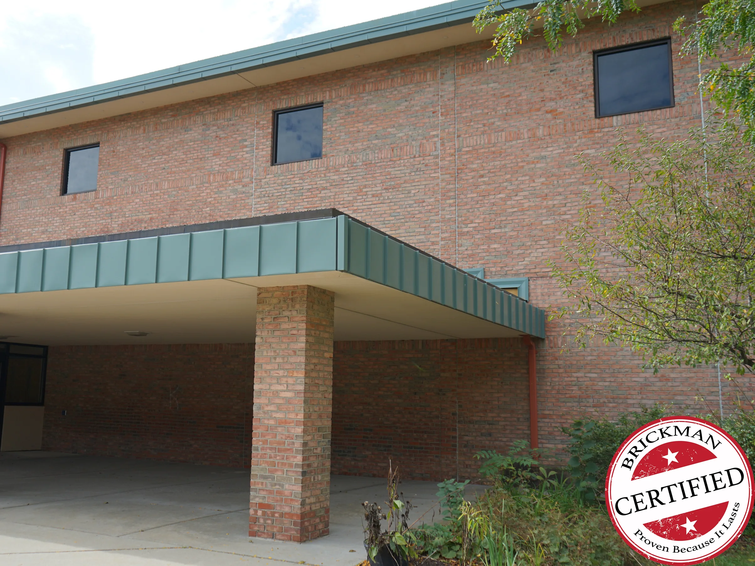 The covered entrance of the school in 2019, a green metal canopy on a brick column with the two-story wall above it reading as one red and tan brick range