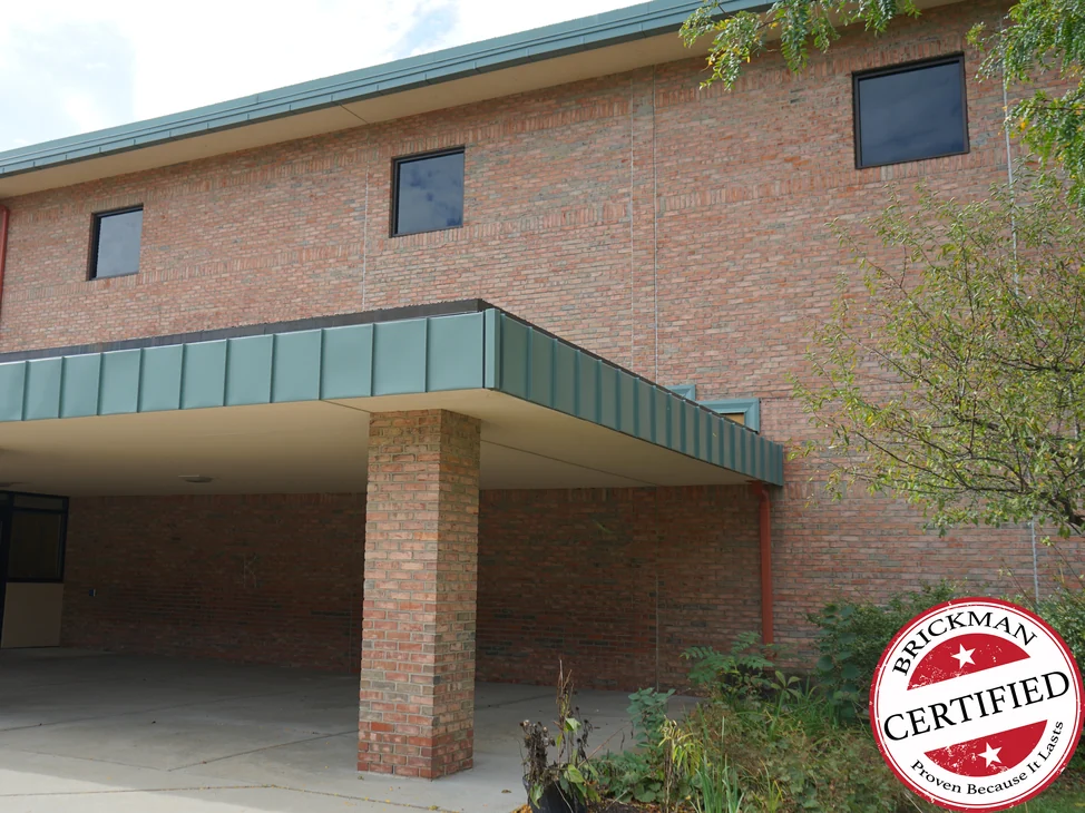 The covered entrance of the school in 2019, a green metal canopy on a brick column with the two-story wall above it reading as one red and tan brick range.