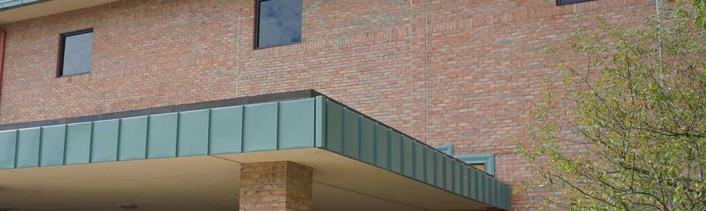 The covered entrance of a Michigan school in 2019, its brick an even red and tan range under a green metal canopy