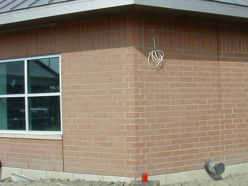The same corner later in 2002 with the shaped units darkened, the corner now carrying the red range of the walls either side, the same coil of wire and the same bare dirt still in place