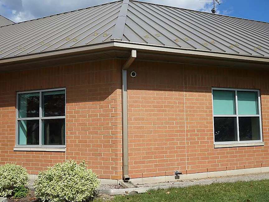 A second corner of the building in 2019, a downspout dropping down the shaped corner between two window bays, the brick reading as one red range from the base course to the eaves