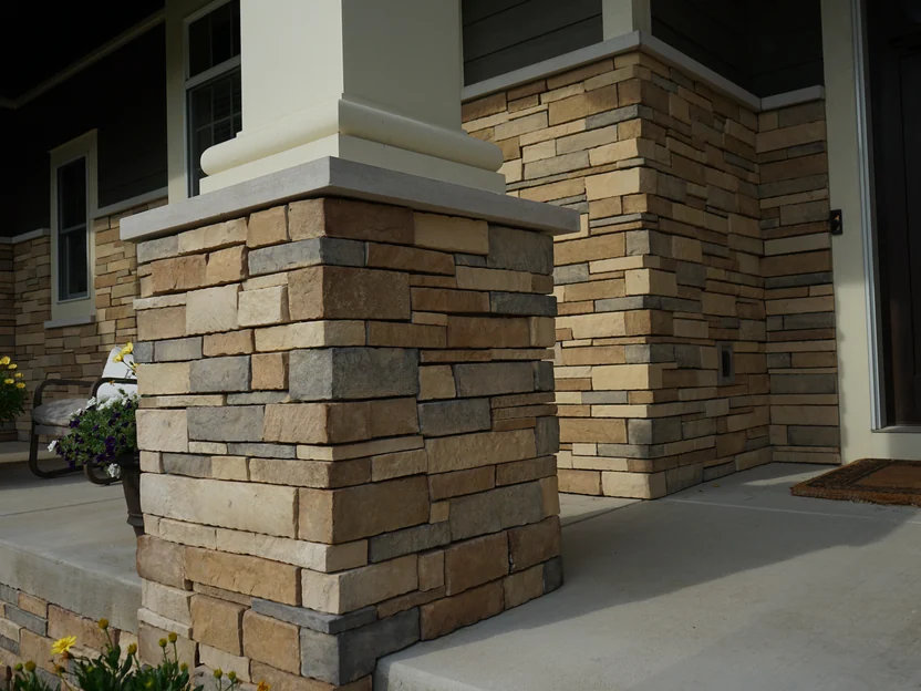 A porch column on its stone pier in 2019, the tan, brown and grey units of the pier under a cast stone cap, the front door beyond