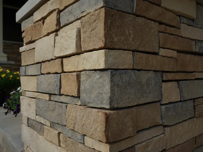 Stone veneer at close range on a pier corner in 2019, individual units in tan, buff, brown and grey with their split faces and shadow lines