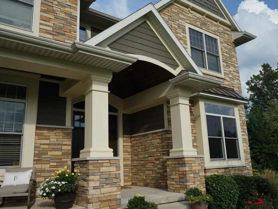 The front entry of the Michigan home in 2019, cream columns on stone piers under a gabled porch, the manufactured stone reading as one tan and grey blend