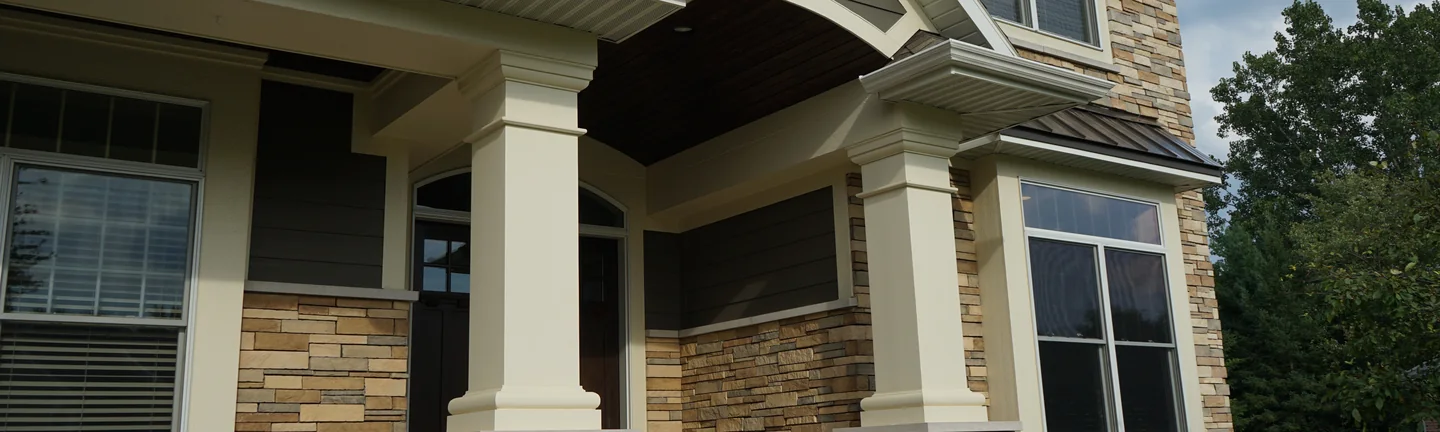 The front entry of the Michigan home in 2019, cream columns on stone piers under a gabled porch, the manufactured stone reading as one tan and grey blend