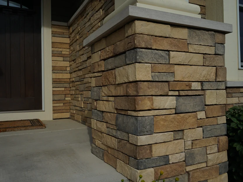 The corner of a stone pier at the front door in 2019, seen close, the ledge stone units in tan, brown and grey under a cast stone cap
