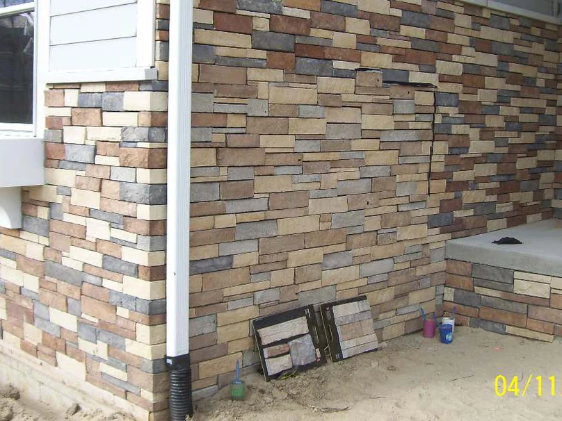 The porch corner in April 2012 with two sample boards of the approved stone blend leaning against the unstained wall, a camera date stamp in the corner