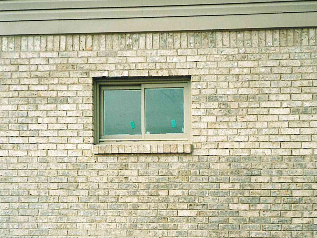 A window in the light brick side wall in 1998, a soldier course under the siding and the units running from cream to pale grey across the coursing