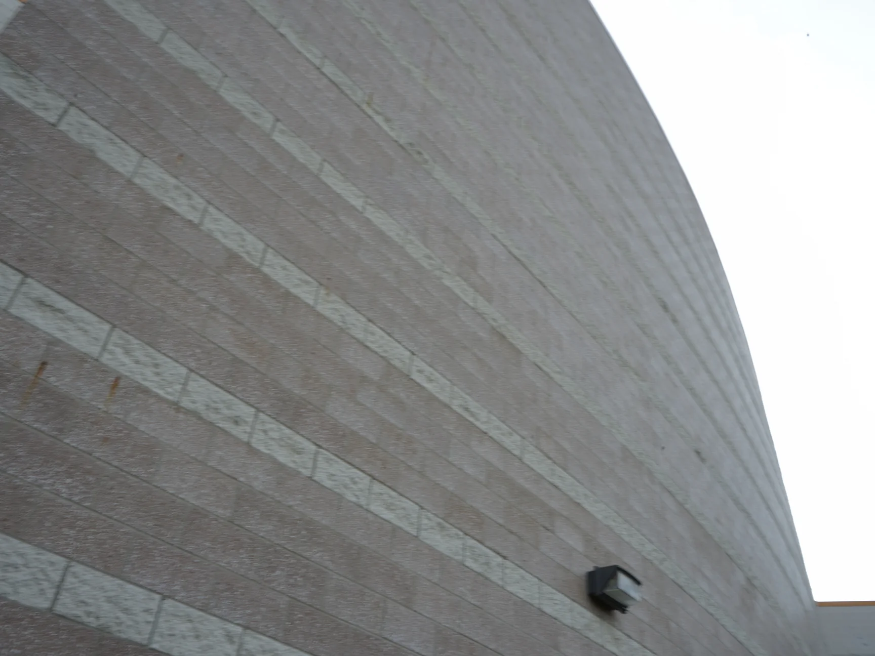 Looking up the curved wall in 2019, pale accent courses raking away across the tan block, the units and the joints reading as one range, with a wall light near the top right