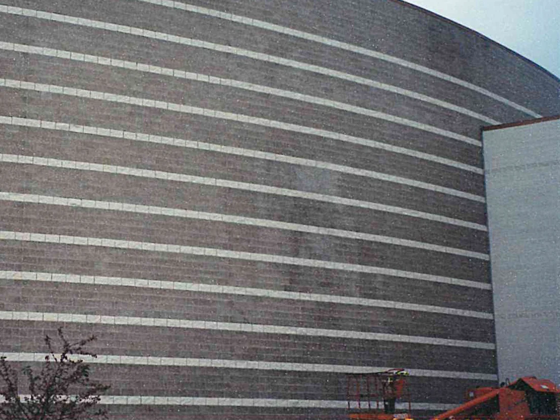 The curved block wall in 2000, pale accent courses banding a darker field, a patch near the middle of the wall reading lighter than the block around it, a boom lift parked at the foot of the wall and the camera date 10 14 '00 burned into the frame