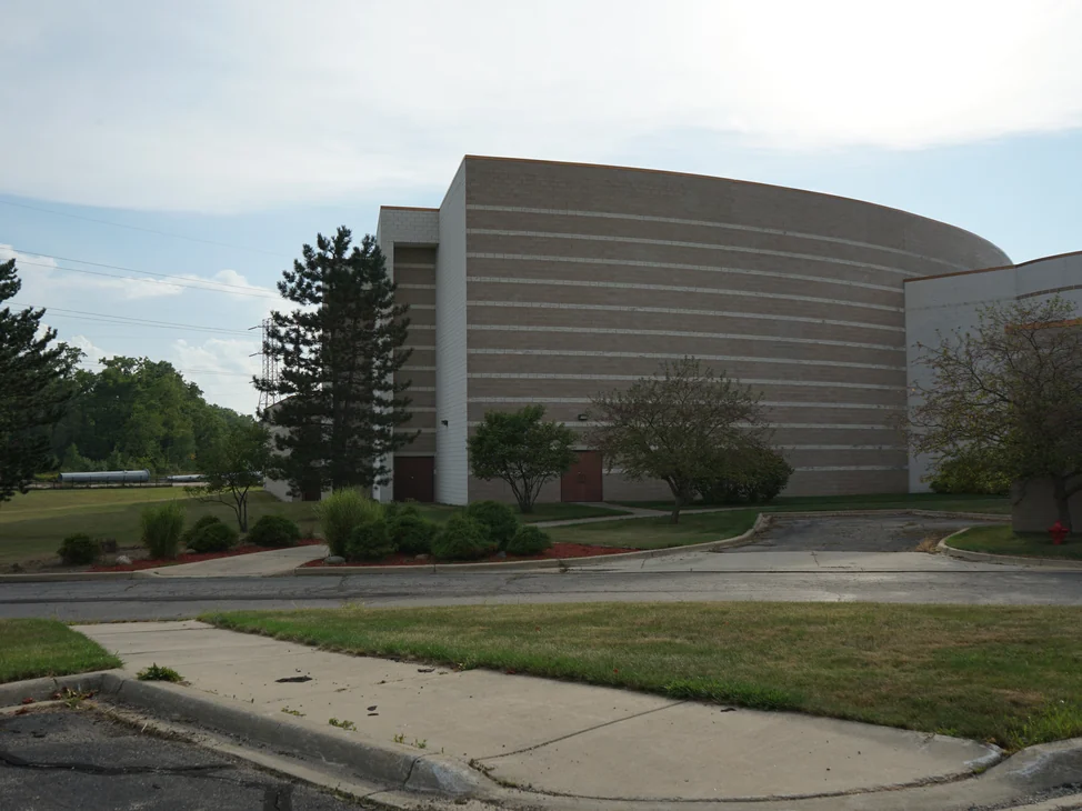 The Michigan temple from the road in 2019, a tall curved block volume with light accent courses stepping across it, joined to a long low wing