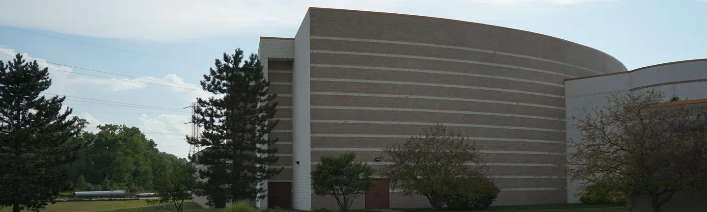 The curved block volume of the Michigan temple in 2019, light accent courses banding the tan wall above a long low wing