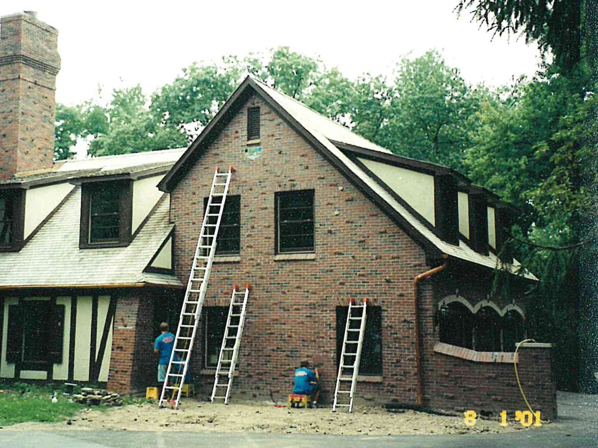 Two applicators on ladders working across the brick gable end of a Tudor house in 2001, the brick a light mottled red beside a half timbered wing