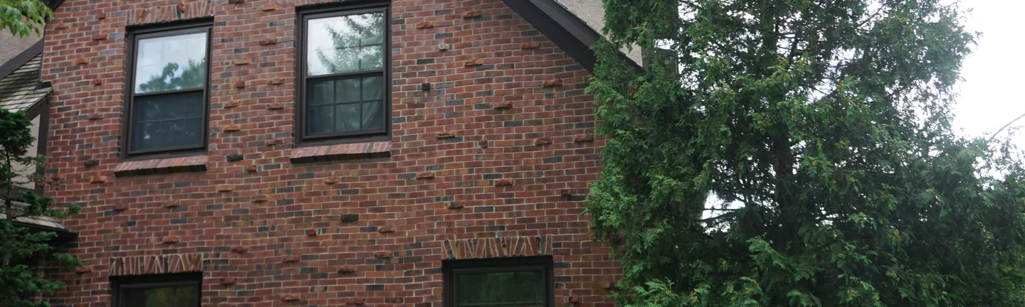 The stained brick of the gable end in 2019, a deep red brown wall with rough rust coloured units projecting from the face