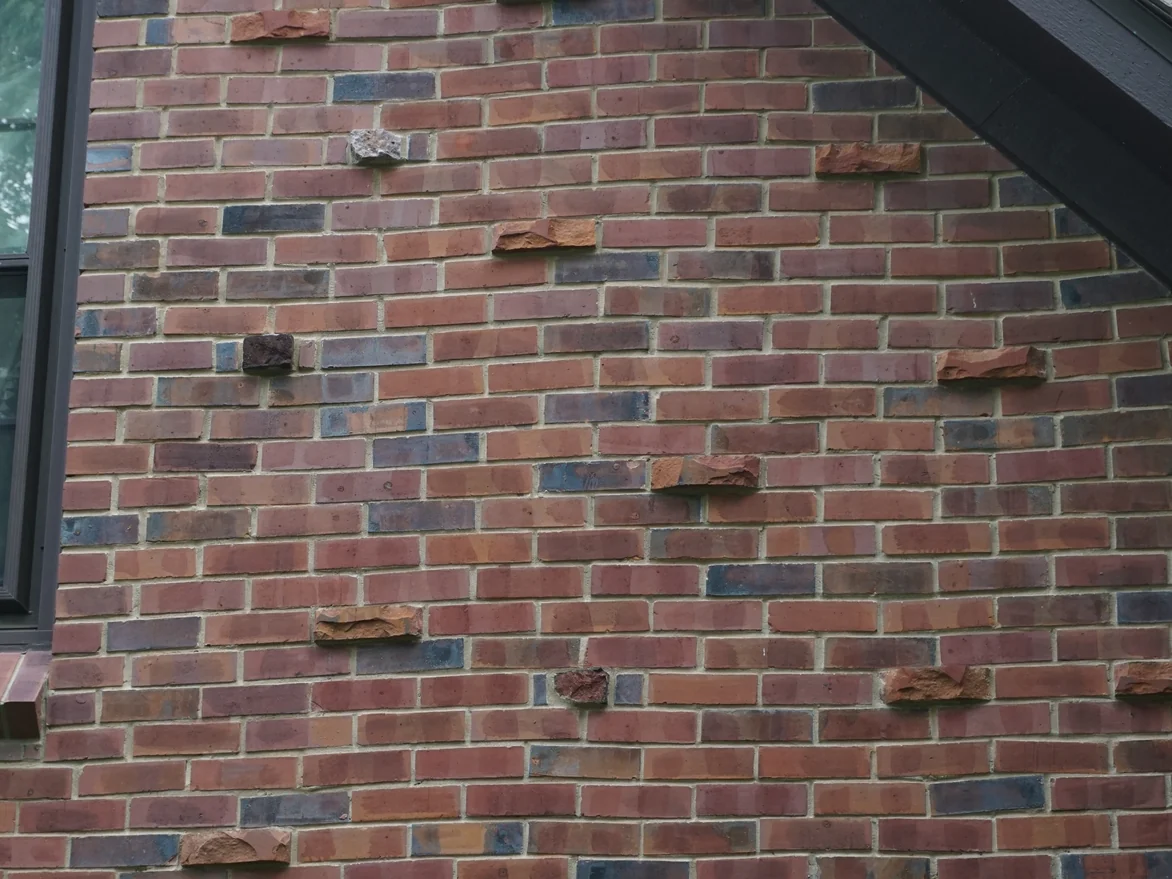 A raking view up the gable wall in 2019, the field brick an even dark red brown with rough rust coloured headers standing proud of the face