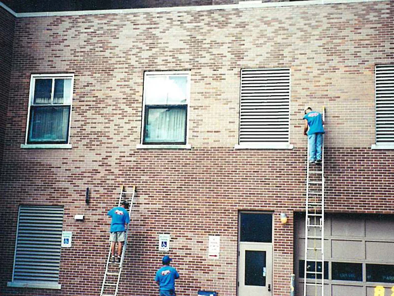 Three applicators on extension ladders working across the rear elevation of the university building in 2000, the upper brick still pale above the darker lower courses