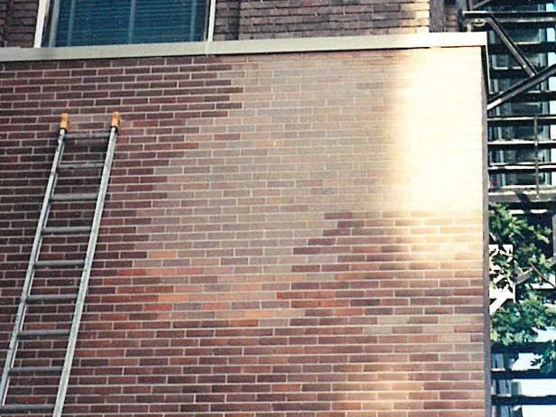 A wall of the university building in 2000 partway through the work, the lower courses darkened to one range and the upper courses still pale, with a ladder against the left side