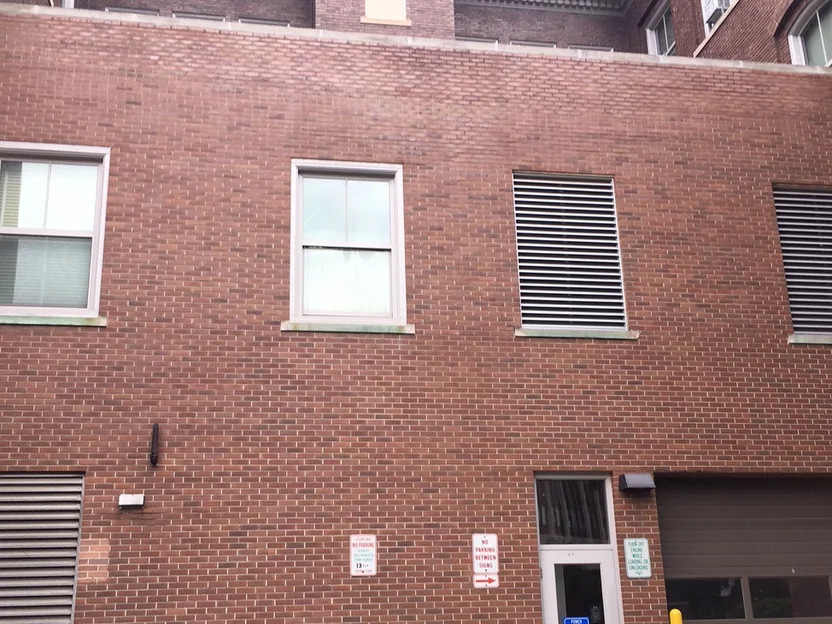The upper wall above the loading dock in 2019, two windows and two louvered vents set in brick that reads as one range