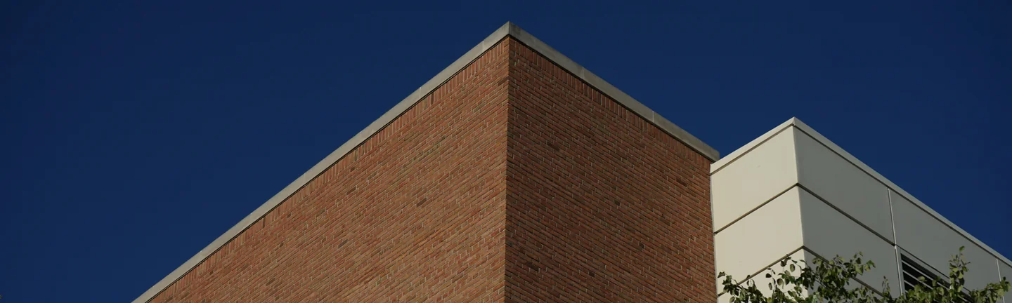 The corner of the university building in 2019, its brick reading as one tan and red range against a deep blue sky