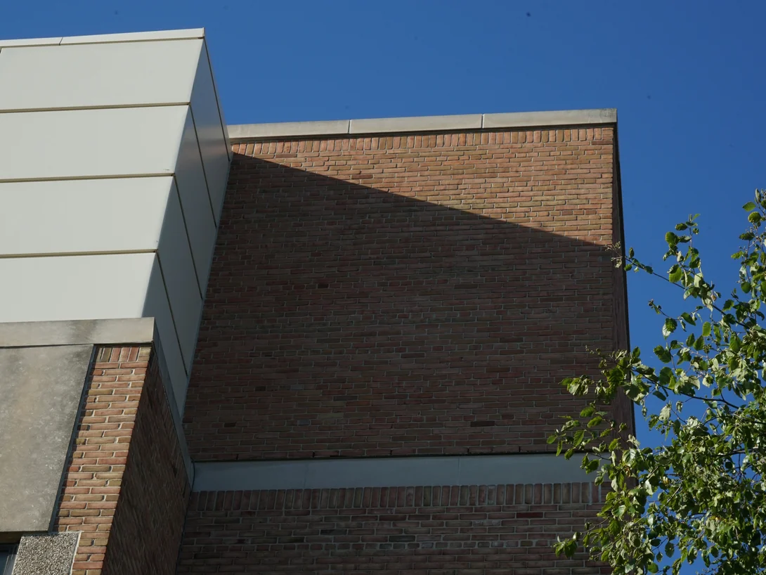 Looking up the corner where the brick meets a cream panel volume, the limestone band and soldier course running across the wall