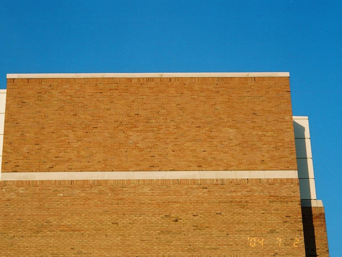 A brick end wall the next day in low evening sun, the band above the limestone course reading in the same tan range as the brick below it