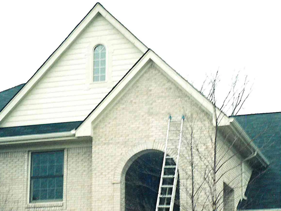 The front of the house in 1998 with an extension ladder standing against the arched entry, the gable brick a flat pale tan