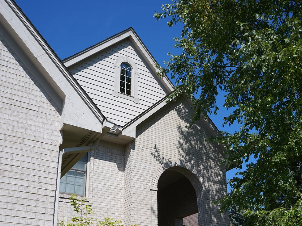 The front of the house in 2019, the white brick running from the dormer gable down past the entry arch as a single range