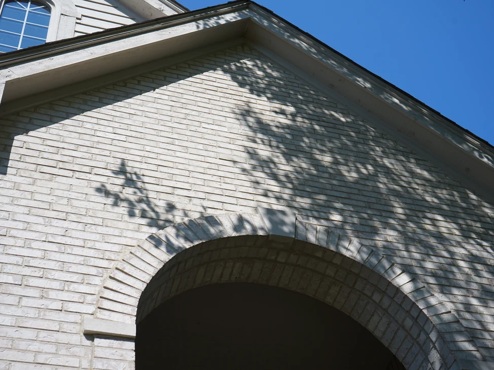 The white brick gable and the head of the entry arch in 2019, one even range of whites under tree shadow.