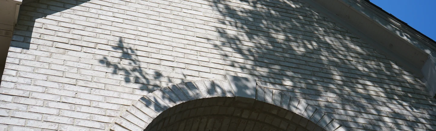 The white brick gable and the head of the entry arch in 2019, one even range of whites under tree shadow