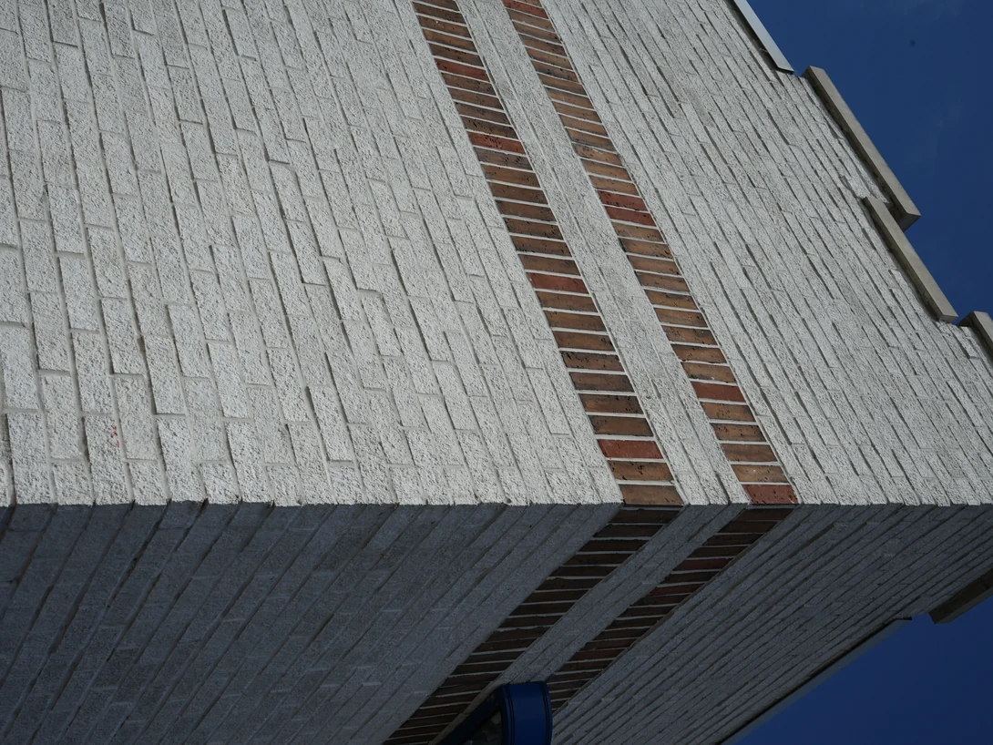 The top of the wall in 2019 seen from below against a deep blue sky, white brick either side of two courses of red and tan banding