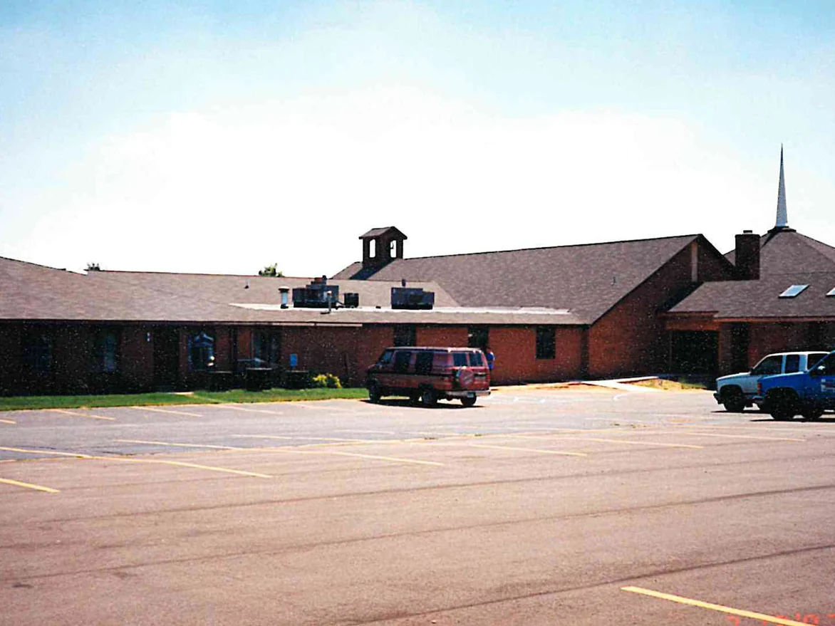 The same wing after staining, the brick and the panels between the windows now reading as one deep red brown, with the sanctuary gable and white steeple at the right