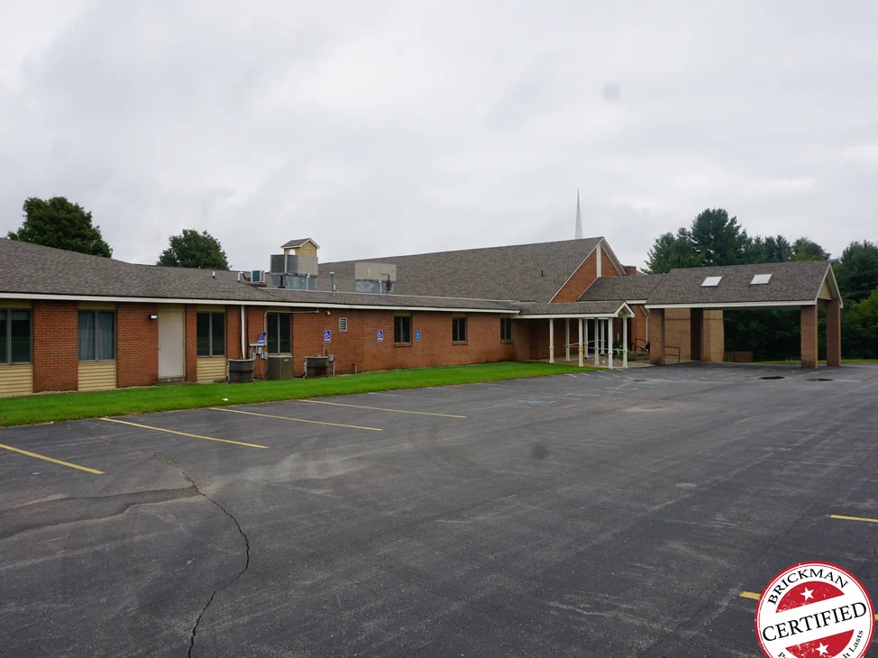 The long brick wing and sanctuary gable of the Middleville church in 2019, reading as one even red brown under an overcast sky, with a covered drop-off at the far end