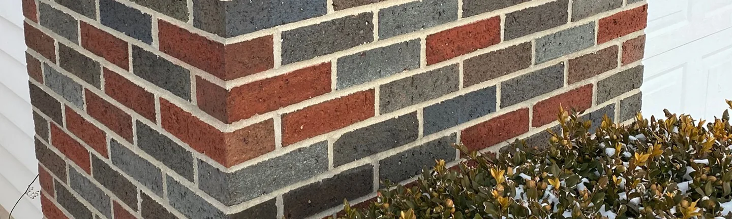 The outside corner of the brick pier at the Midland home in 2021, red and flashed blue grey brick in one range beside white siding