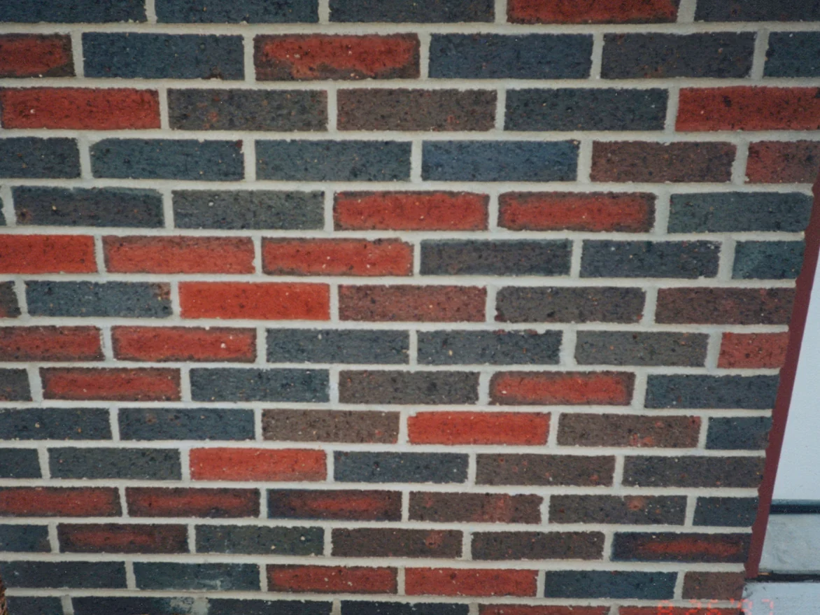 The face of the brick pier in August 1997 before staining, flashed grey and dull red units in pale mortar beside a maroon door frame, with the camera date 8/26/97 burned in