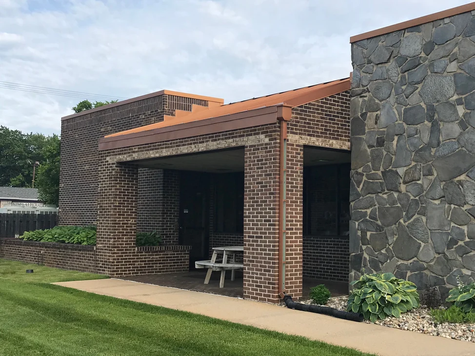 The entrance bay in 2019, its brick columns a red brown under a copper fascia with the fieldstone wall at the right