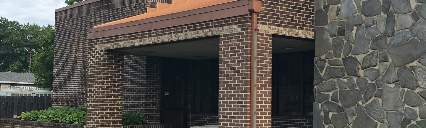 The credit union entrance in 2019, brick columns and a copper fascia beside a fieldstone wall