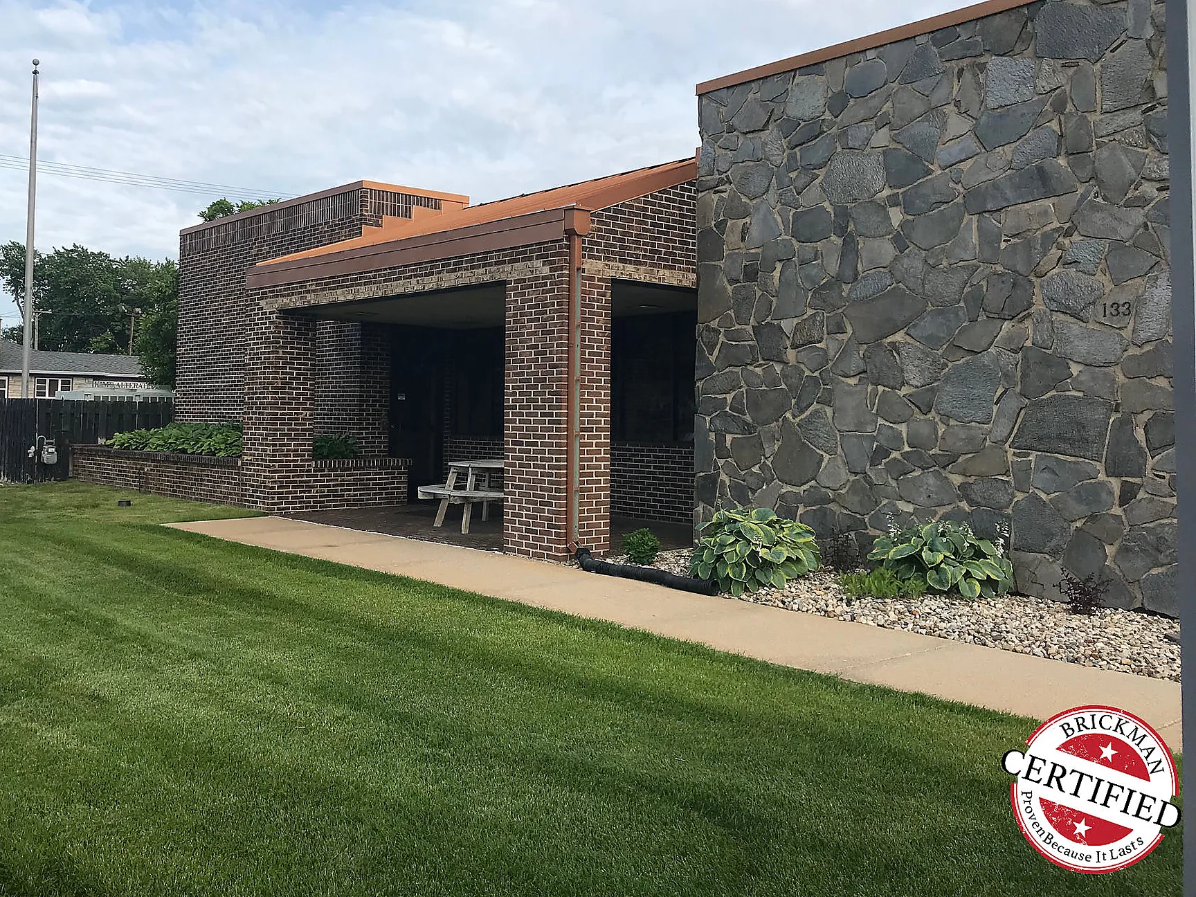 The branch from the front lawn in 2019, the entrance bay and the fieldstone wall under a low copper roofline