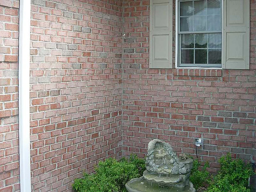 The inside corner of the house in 2007, two walls of dark red brick meeting behind a stone fountain and a low green shrub, a shuttered window above