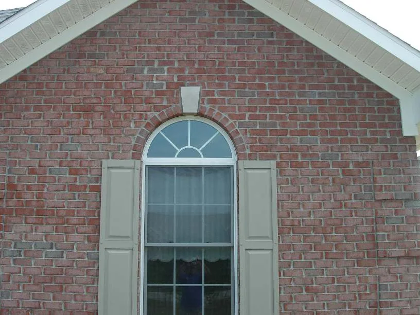 The front gable in 2007, an arched fanlight window between shutters, the brick around it dark red and patched with darker blotches