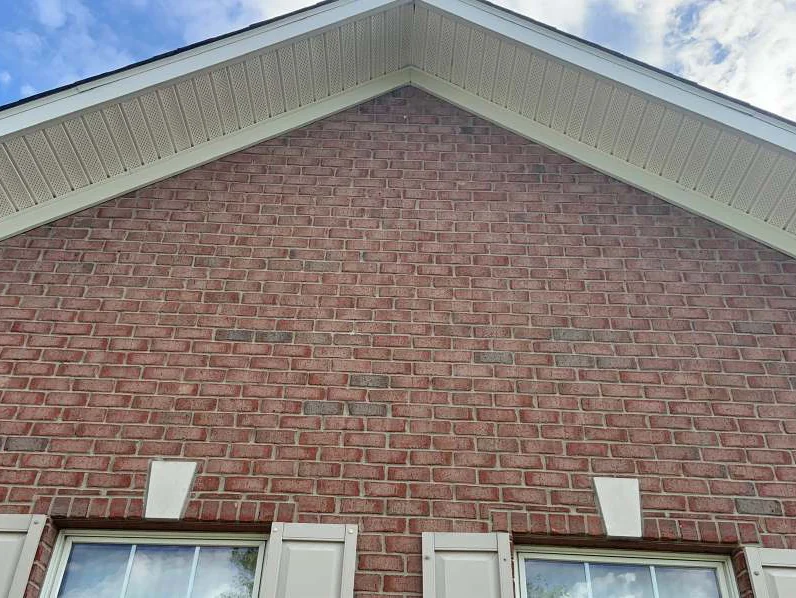 The same gable peak in 2019, the brick holding one salmon range across the courses under a blue sky
