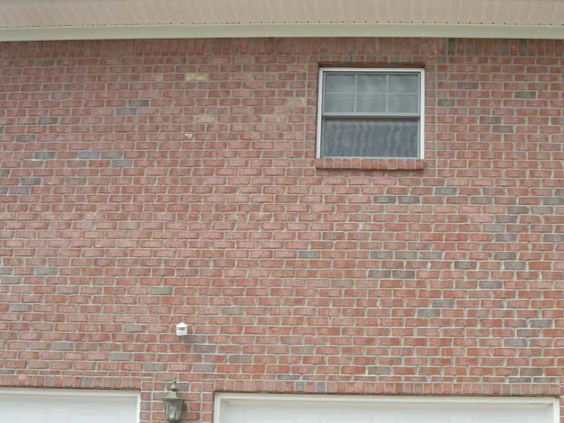 The wall above the garage doors in 2007, a single window in a broad field of dark red brick with uneven darker courses running through it