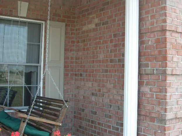The covered porch in 2007, a wooden swing on chains and red geraniums against dark red brick walls